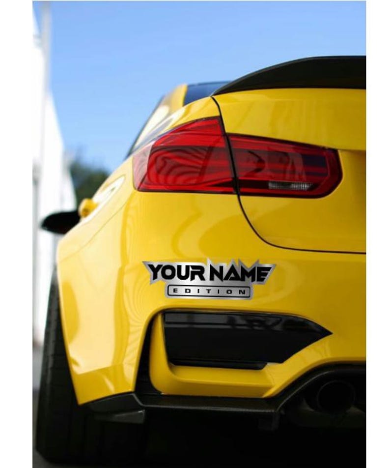 Puede incluir: Un coche amarillo con un aler&oacute;n negro y una calcoman&iacute;a plateada que dice "YOUR NAME EDITION".
