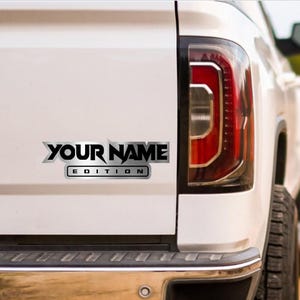 Puede incluir: Una camioneta blanca con una calcoman&iacute;a plateada y negra que dice "YOUR NAME EDITION".