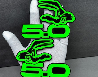 May include: Two green and black 5.0 logo stickers featuring a cartoon rabbit with a racing theme. The stickers are held by a gloved hand against a dark gray background. The text "5.0" is in a bold, neon green font.