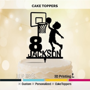 May include: Black cake topper featuring a basketball hoop, a boy silhouette, the number 8, and the name "JACKSON". The words "CAKE TOPPERS" and "Julie Weiss" are also visible. The topper is designed for a cake.