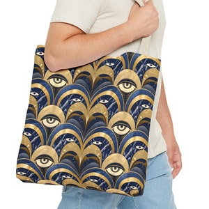 May include: A blue and gold tote bag with a repeating pattern of stylized eyes. The bag has a canvas texture and is being held by a person.