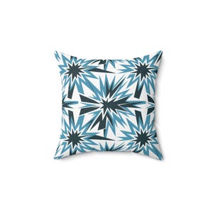 May include: A white throw pillow with a blue and black geometric pattern of stars. The pillow is square and has a soft, plush feel.