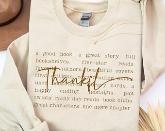 Könnte beinhalten: Ein sandfarbenes Sweatshirt mit Rundhalsausschnitt, das eine Liste buchbezogener Phrasen in Schreibmaschinenschrift zeigt, wobei das Wort Thankful in einer großen, dunkelbraunen Schreibschrift über den Text gedruckt ist.