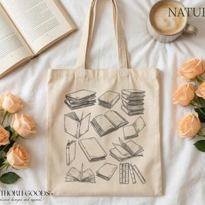 May include: A cream-coloured canvas tote bag with a black and white sketch of books. The bag has long handles and the word "NATURAL" is visible. Peach-coloured roses and an open book are also in the image.