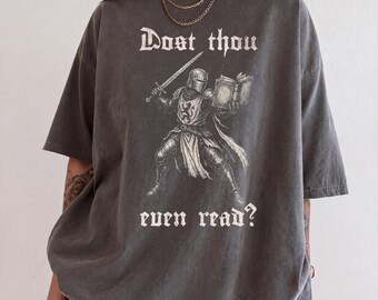 Könnte beinhalten: Ein anthrazitfarbenes Kurzarm-T-Shirt mit einer Grafik eines mittelalterlichen Ritters in Rüstung, der ein Schwert und ein offenes Buch hält. Der Text "Dost thou even read?" ist in weißer gotischer Schrift über und unter dem Ritter gedruckt.