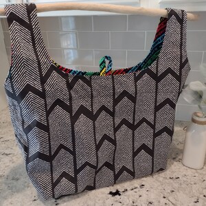 May include: A black and white chevron patterned reusable shopping bag with a colourful fabric lining. The bag is hanging from a wooden dowel.
