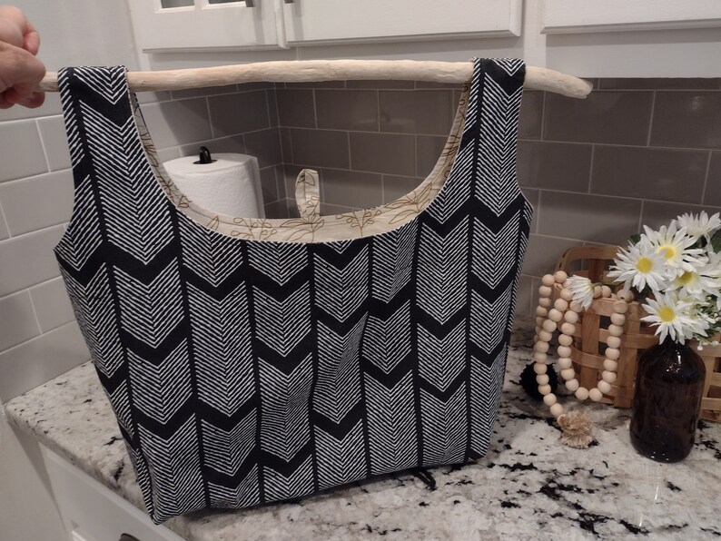 May include: A black and white chevron patterned tote bag with a wooden dowel rod handle. The bag is hanging on a shelf in a kitchen.
