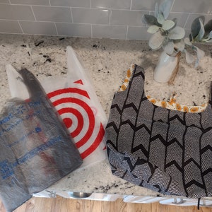 May include: Three reusable shopping bags. Two are plastic bags with the logos "Walmart Pay" and "Target" printed on them. The third bag is a black and white fabric bag with a chevron pattern.