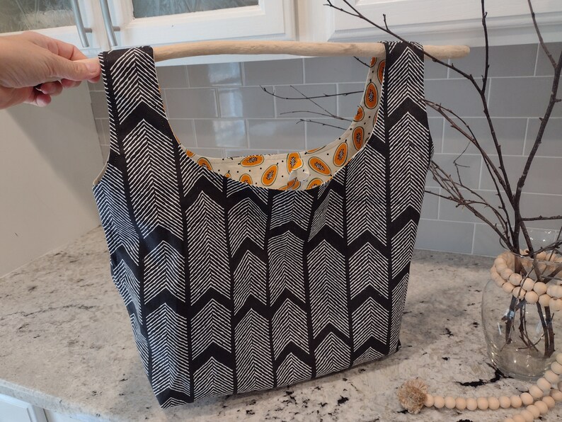 May include: A black and white chevron patterned tote bag with a papaya print lining. The bag has a wooden handle.