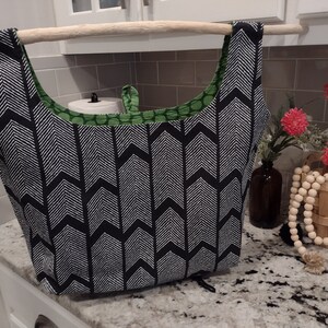 May include: A black and white chevron patterned reusable shopping bag with green polka dot fabric lining. The bag is hanging from a wooden dowel.