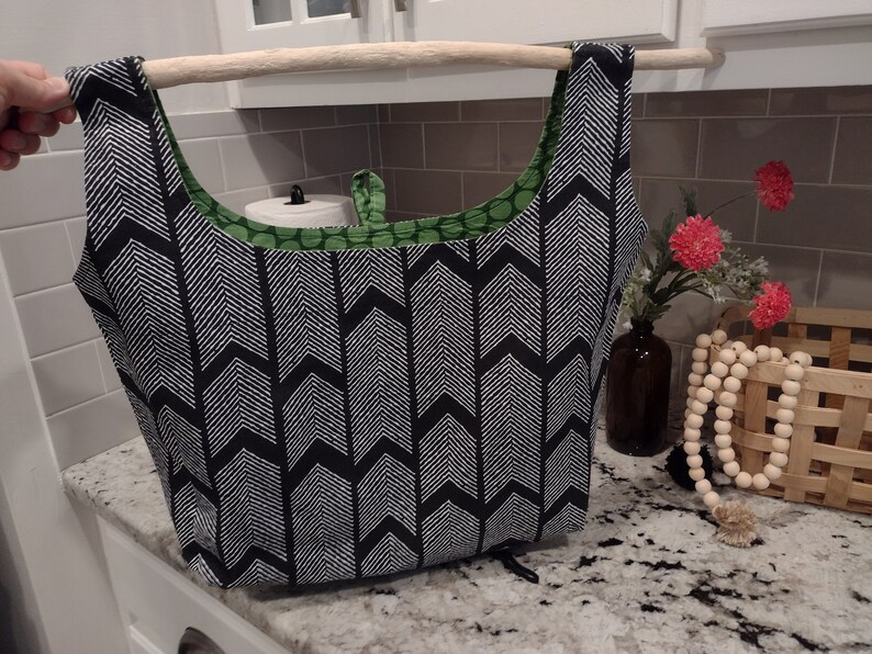 May include: A black and white chevron patterned reusable shopping bag with green polka dot fabric lining. The bag is hanging from a wooden dowel.
