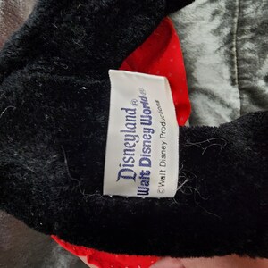 Puede incluir: Peluche negra y roja con una etiqueta blanca que dice "Disneyland&reg; Walt Disney World&reg; &copy; Walt Disney Productions".