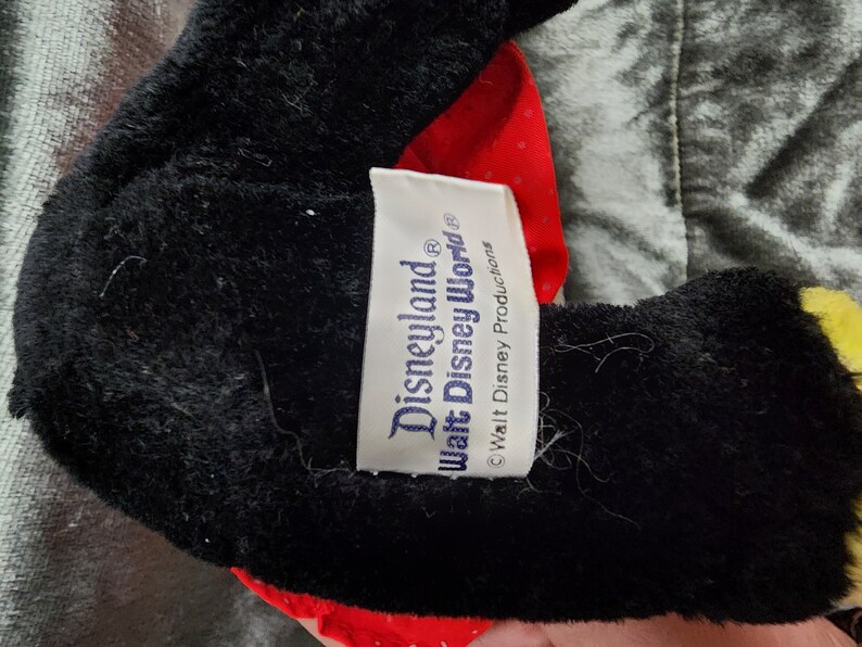 Puede incluir: Peluche negra y roja con una etiqueta blanca que dice "Disneyland&reg; Walt Disney World&reg; &copy; Walt Disney Productions".