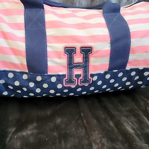 May include: A pink and white striped duffel bag with blue polka dots and a navy blue embroidered letter H on the front.