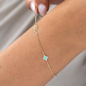May include: A gold chain bracelet with a turquoise blue clover charm and a wing charm.