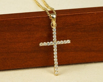 Könnte beinhalten: Eine goldene Kettenkette mit einem kleinen, diamantbesetzten Kreuzanhänger. Die Kette liegt auf einer Holzoberfläche.