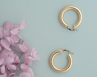May include: Two gold hoop earrings on a light blue background. The earrings are simple and classic, with a smooth, polished finish.