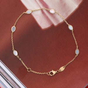 Op de afbeelding: Een fijne gouden kettingarmband met zes gelijkmatig verdeelde, kleine ovale inlays van wit parelmoer. De armband is voorzien van een karabijnsluiting en een klein, glad, ovaalvormig gouden plaatje bij het sluitingsmechanisme.