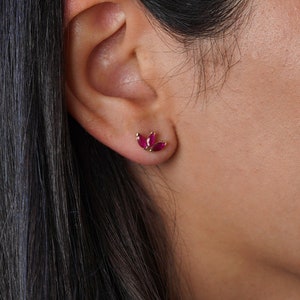 Op de afbeelding: Een paar gouden oorbellen met elk drie kleine robijnrode stenen.