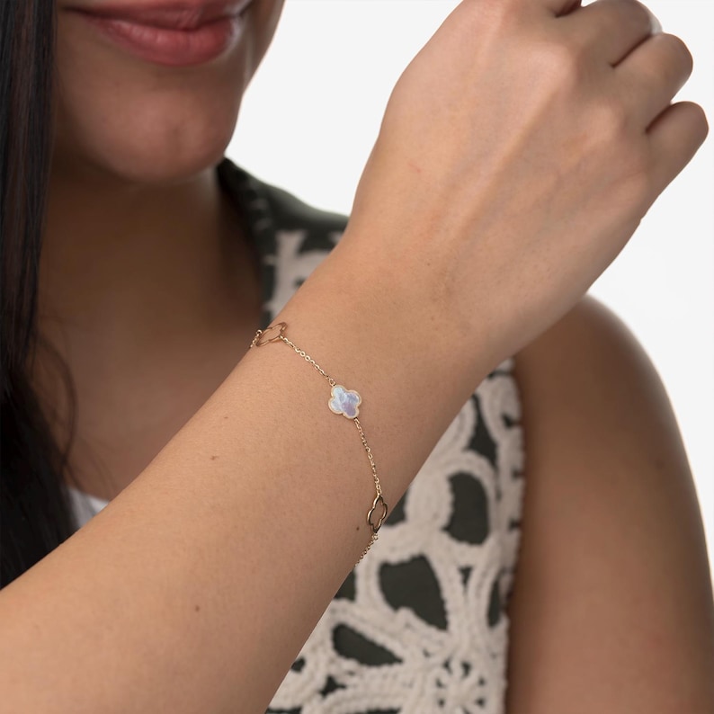 Puede incluir: Un delicado brazalete de oro con un dije de flor de n&aacute;car blanco. El brazalete est&aacute; hecho de una cadena fina y tiene un dise&ntilde;o simple y elegante.