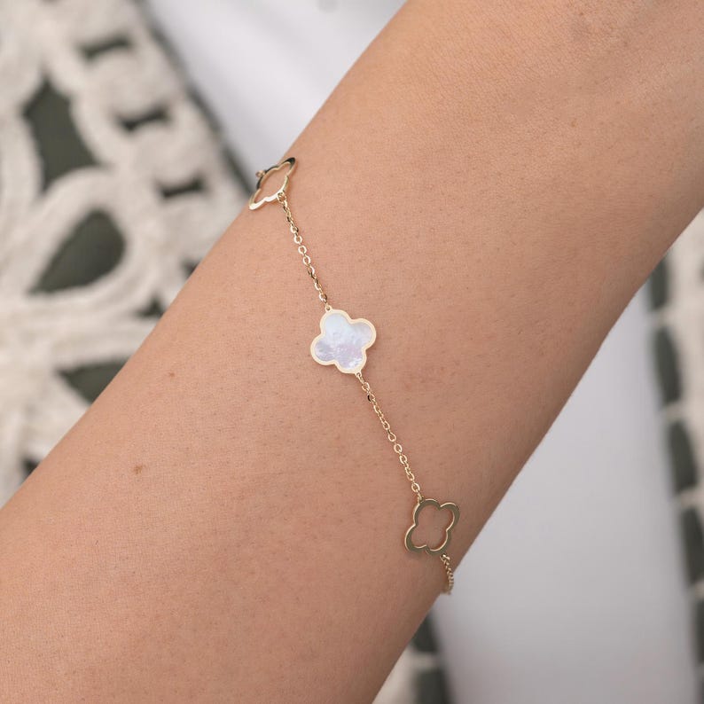 Puede incluir: Un brazalete de cadena dorada con cuatro dijes en forma de tr&eacute;bol. Dos de los dijes est&aacute;n rellenos de n&aacute;car blanco.