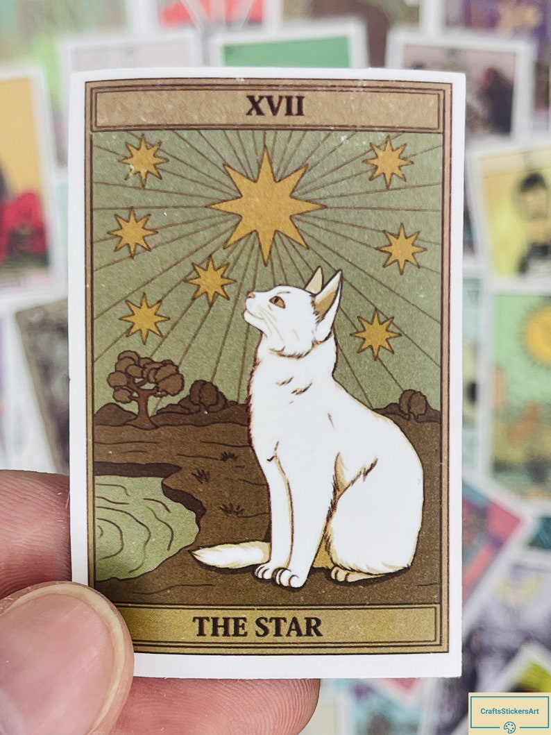 May include: A vintage tarot card with a white cat sitting on a brown rock, looking up at a large yellow star with smaller stars around it. The card is green and brown with the text "XVII THE STAR" at the bottom.