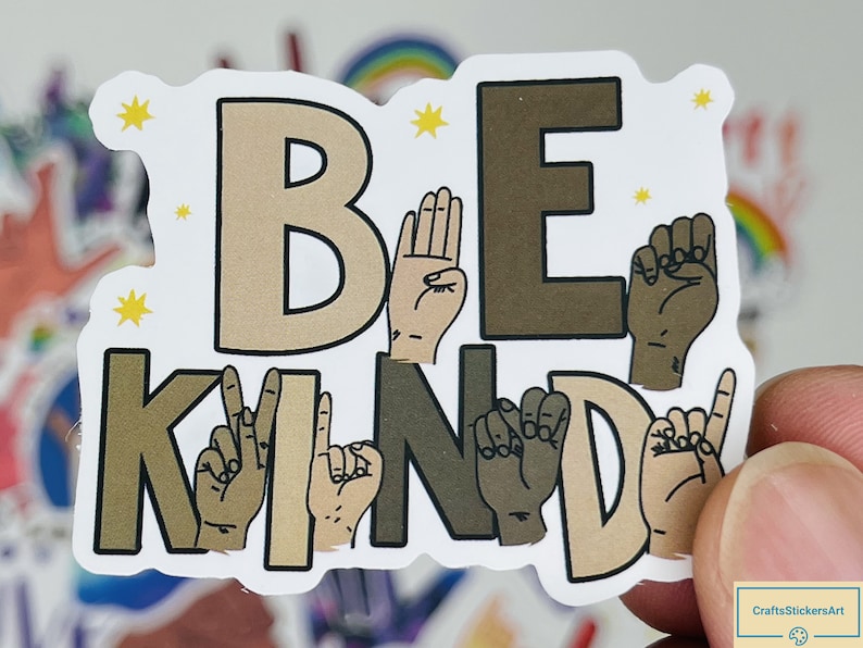 May include: A white sticker with the words "Be Kind" in brown and beige letters. The letters are formed by hands signing the letters in British Sign Language.