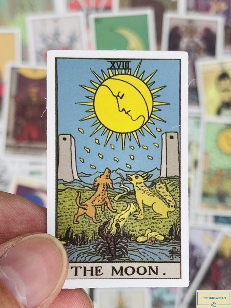 May include: The Moon tarot card, featuring a yellow moon with a face, two towers, two dogs, and a scorpion. The card is blue with a green border and the text "THE MOON."