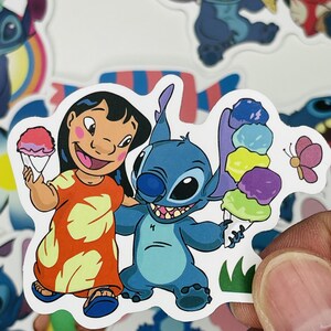 Puede incluir: Una pegatina con Lilo y Stitch de la pel&iacute;cula de Disney Lilo & Stitch. Lilo lleva un vestido rojo y amarillo y sostiene un hielo raspado azul, rosa y blanco. Stitch lleva su caracter&iacute;stico pelaje azul y sostiene un hielo raspado multicolor. La pegatina est&aacute; sobre un fondo blanco.