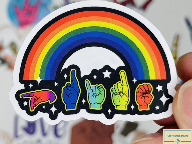May include: A rainbow sticker with a black background and five hands signing the word "love" in American Sign Language. The hands are outlined in black and have a rainbow colour scheme. The sticker has a white border.