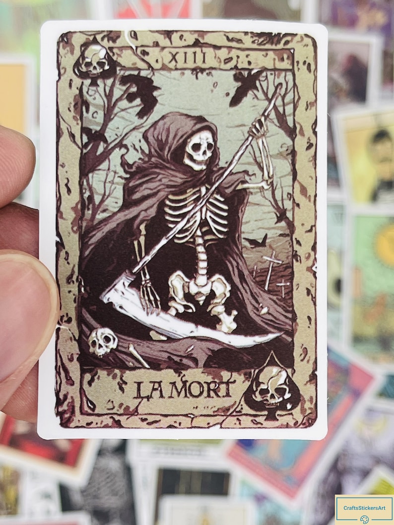 May include: A vintage-style tarot card featuring Death, the 13th card in the Major Arcana. The card depicts a skeletal figure in a hooded robe, holding a scythe and standing in a graveyard. The card is labeled "La Mort" in a decorative font.