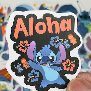 Puede incluir: Una pegatina azul del personaje Stitch con la palabra "Aloha" en letras rojas sobre un fondo negro. La pegatina presenta a Stitch con una expresi&oacute;n amigable, rodeado de flores de hibisco y figuras tiki.