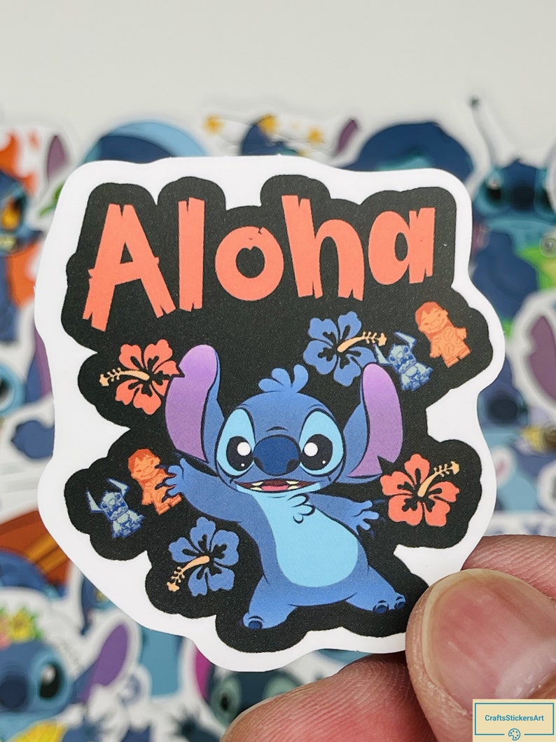 Puede incluir: Una pegatina azul del personaje Stitch con la palabra "Aloha" en letras rojas sobre un fondo negro. La pegatina presenta a Stitch con una expresi&oacute;n amigable, rodeado de flores de hibisco y figuras tiki.