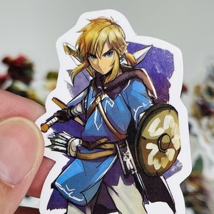 May include: A sticker featuring a cartoon illustration of Link from the Legend of Zelda video game series. Link is wearing a blue tunic, brown trousers, and a green cap. He is holding a sword and shield. The background is a purple watercolour wash.