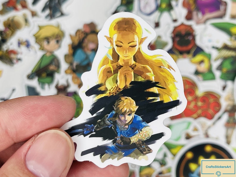 May include: A sticker featuring a watercolour-style illustration of Link and Zelda from the Legend of Zelda video game series. Link is in the foreground, wearing blue and green armour, and Zelda is in the background, with long blonde hair and a white dress.