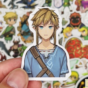 May include: A sticker featuring a cartoon illustration of Link from the Legend of Zelda video game series. Link is wearing a blue tunic with a brown strap and has blonde hair and blue eyes.