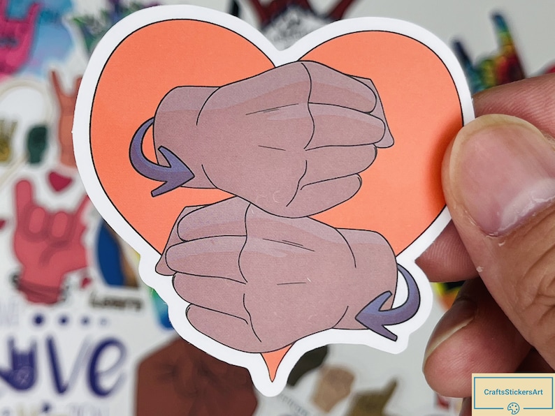May include: A heart-shaped sticker with two hands forming the British Sign Language symbol for "love". The hands are brown and the heart is orange.