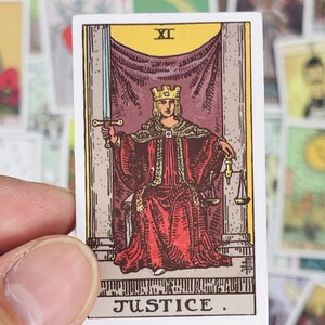 May include: A tarot card with a white background and a colorful illustration of a figure wearing a crown and red robe holding a sword and scales. The card is labeled "Justice" and "XI".