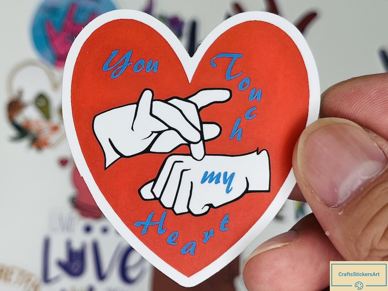 May include: Red heart-shaped sticker with a white outline. The sticker features two hands signing "You touch my heart" in British Sign Language. The text is in blue.