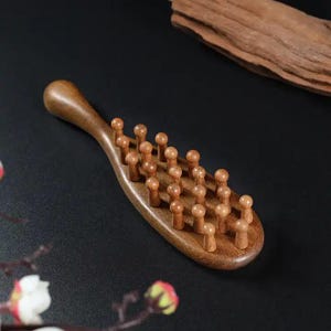 Op de afbeelding: Een houten massagegereedschap met een handvat en afgeronde pinnen. Het gereedschap is gemaakt van lichtbruin hout en is ontworpen voor massage. De handgreep is gebogen voor een gemakkelijke grip.