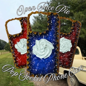 May include: Three phone cases with a pie design. The cases have a red, blue, and red filling, with a white swirl of whipped cream. The cases are edged with a golden crust. The text "Open Face Pie" and "Pop Socket Phone Case" are written on the image.