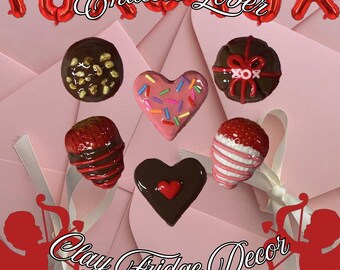 May include: A collection of Valentine's Day-themed clay fridge magnets. The magnets include heart shapes, strawberries, and round chocolates, decorated with sprinkles, nuts, and chocolate drizzle. The image includes the text "Endless Lover" and "Clay Fridge Decor".