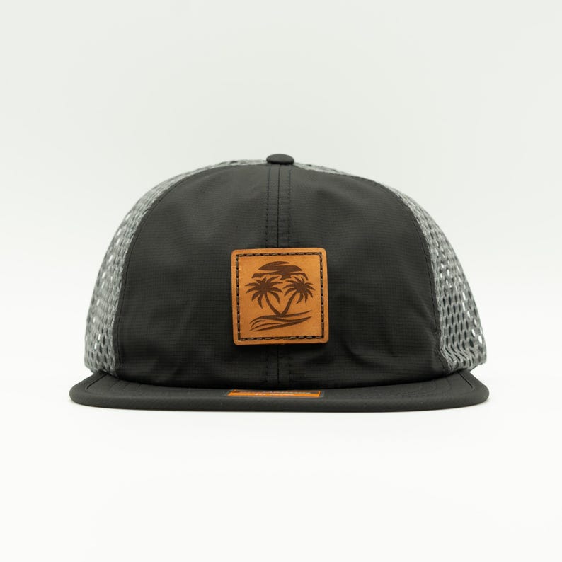 May include: A black and gray mesh baseball cap with a brown leather patch featuring a palm tree design.