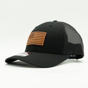 Add a patriotic touch to your look with our black/black Richardson 115 or 112 hat. Featuring a hand-sewn American flag leather patch, adjustable Snapback, and made in Colorado, USA for quality you can trust! Trucker cap with mesh back.