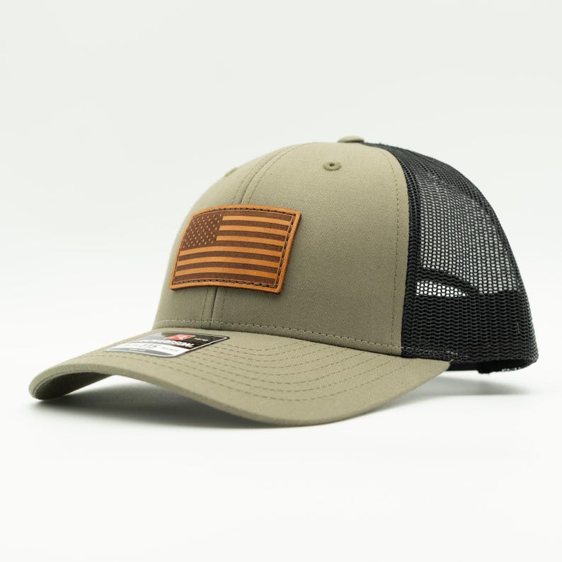 Add a patriotic touch to your look with our Loden Green and black Richardson 115 or 112 hat. Featuring a hand-sewn American flag leather patch, adjustable Snapback, and made in Colorado, USA for quality you can trust! Trucker cap with mesh back.