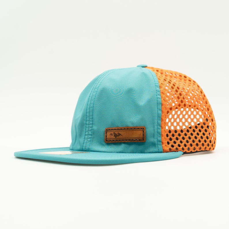Side view of teal Richardson 935 performance hat with bright orange mesh and leather Active Mountain patch, lightweight packable water resistant outdoors hat for hiking and travel