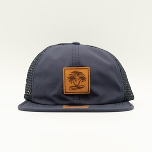 May include: A navy blue mesh trucker hat with a brown leather patch featuring a palm tree design.