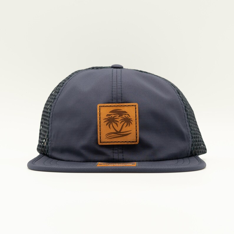 May include: A navy blue mesh trucker hat with a brown leather patch featuring a palm tree design.