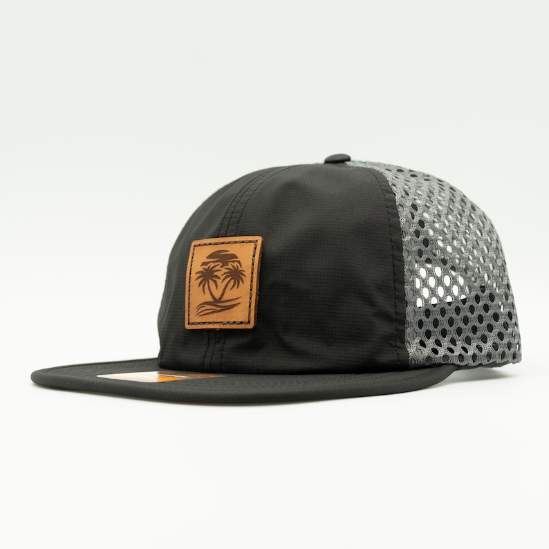 May include: Black and gray mesh baseball cap with a brown leather patch featuring a palm tree design.