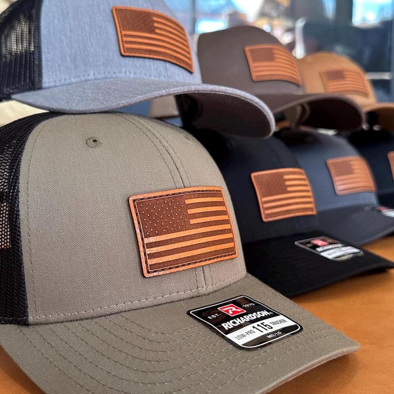 Add a patriotic touch to your look with our Carmel and black Richardson 115 hat. Featuring a hand-sewn American flag leather patch, adjustable Snapback, and made in Colorado, USA for quality you can trust! Quality Trucker cap with mesh back.